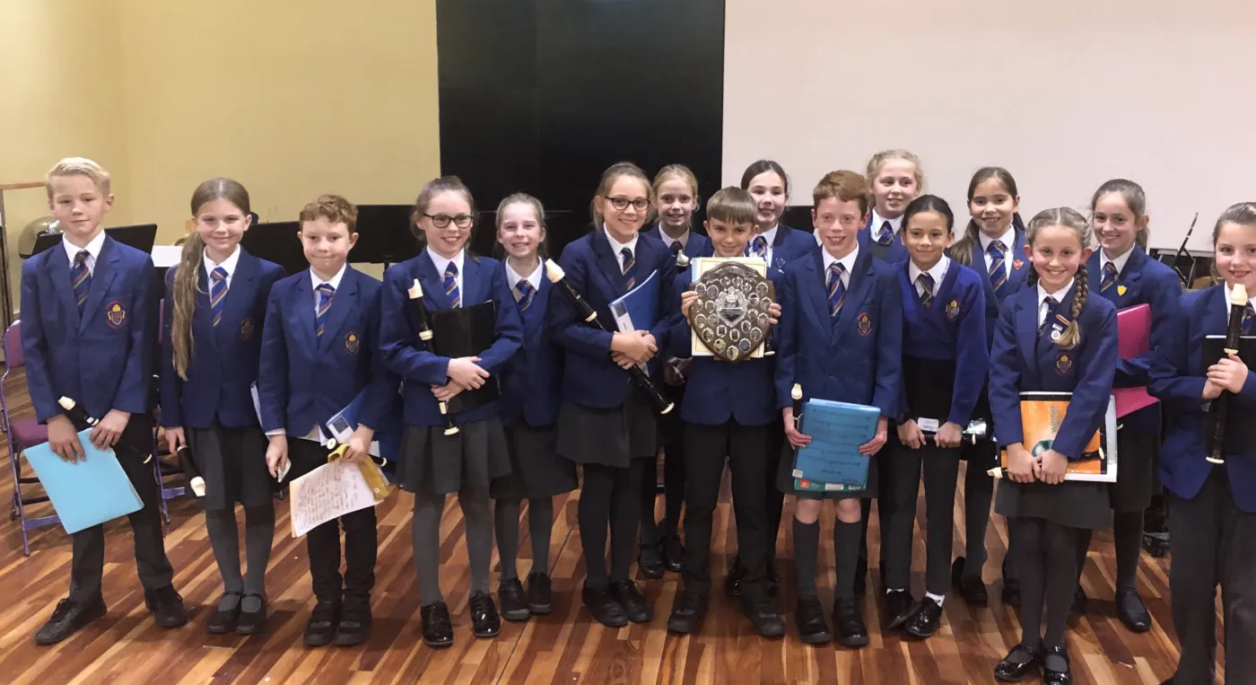 A school recorder group with a festival shield, in a photograph Woking Music Festival publishes on its own website. It shows an earlier year's festival, not 2026